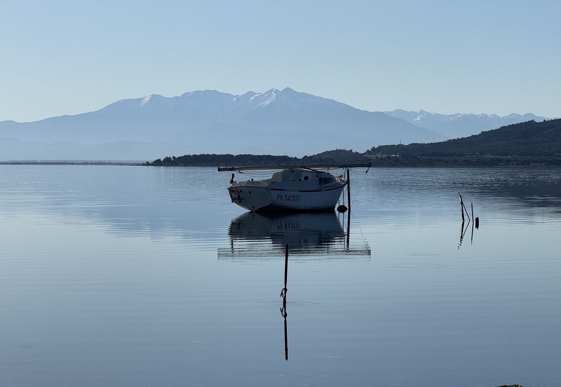 A small boat is peacefully anchored on a calm lake with mountains in the background.