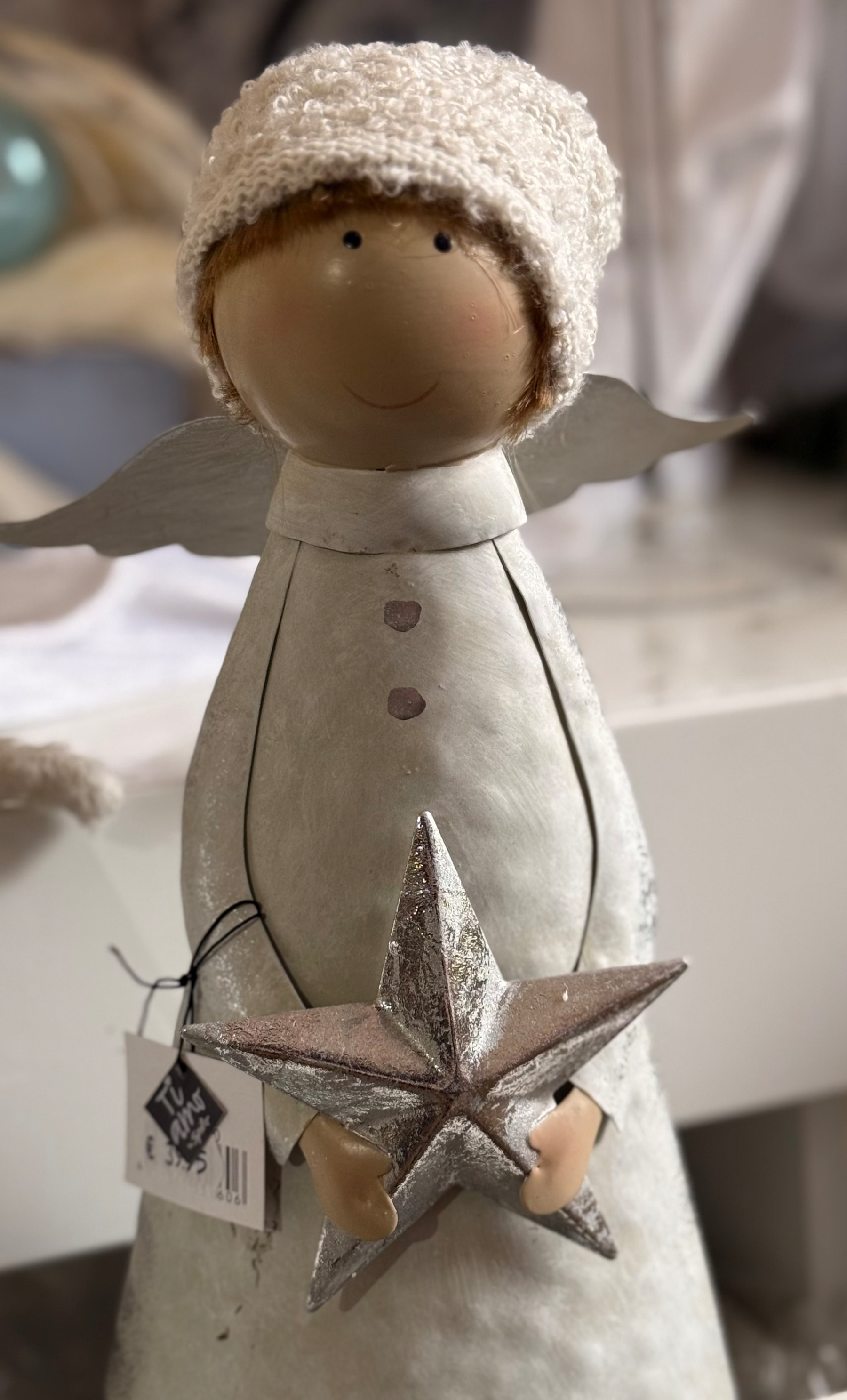 A cute angel figurine, for sale in a shop, wearing a knitted hat holds a metallic star. 