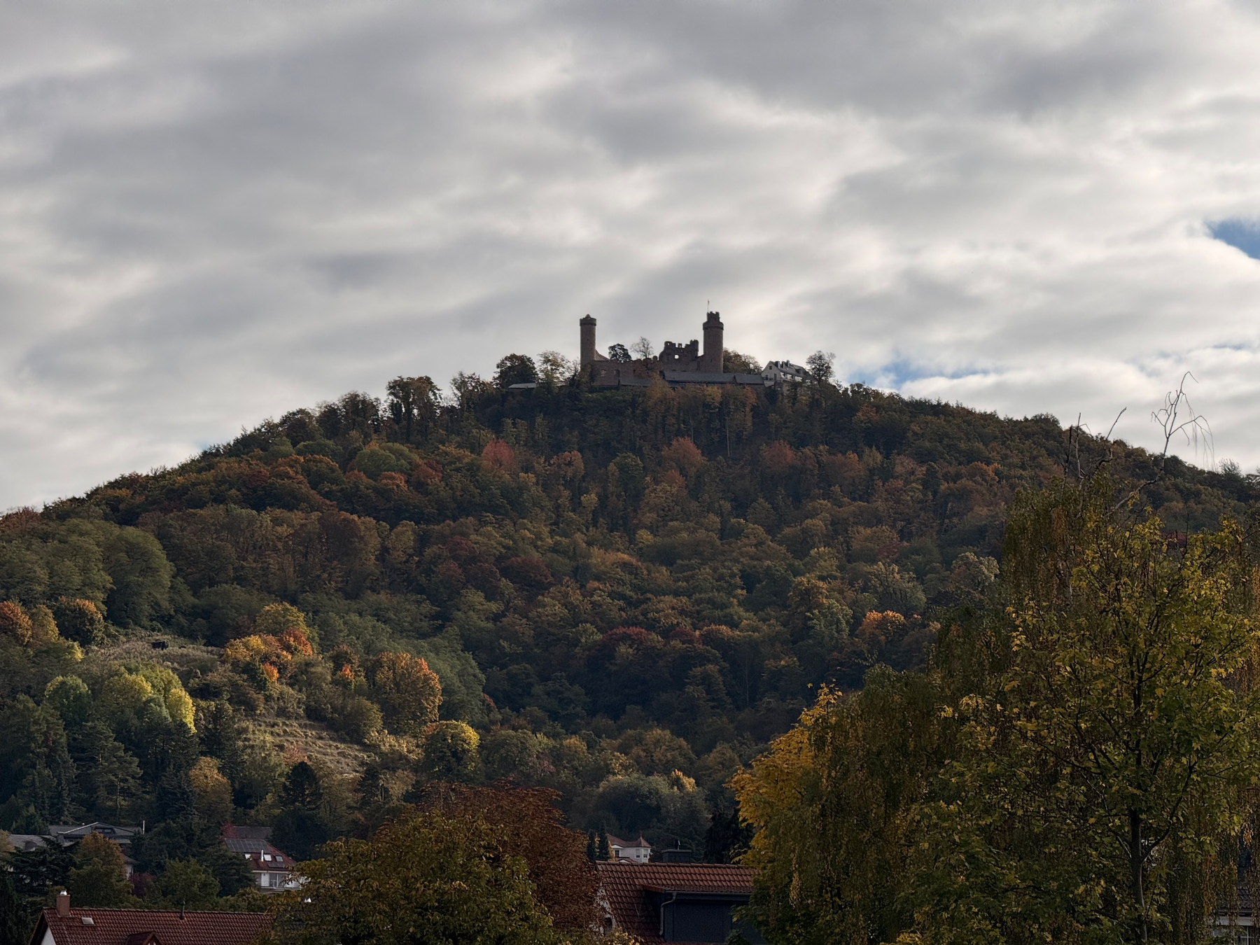 Auerbach Castle sits atop a tree-covered hill under a cloudy sky, surrounded by signs of autumn foliage.