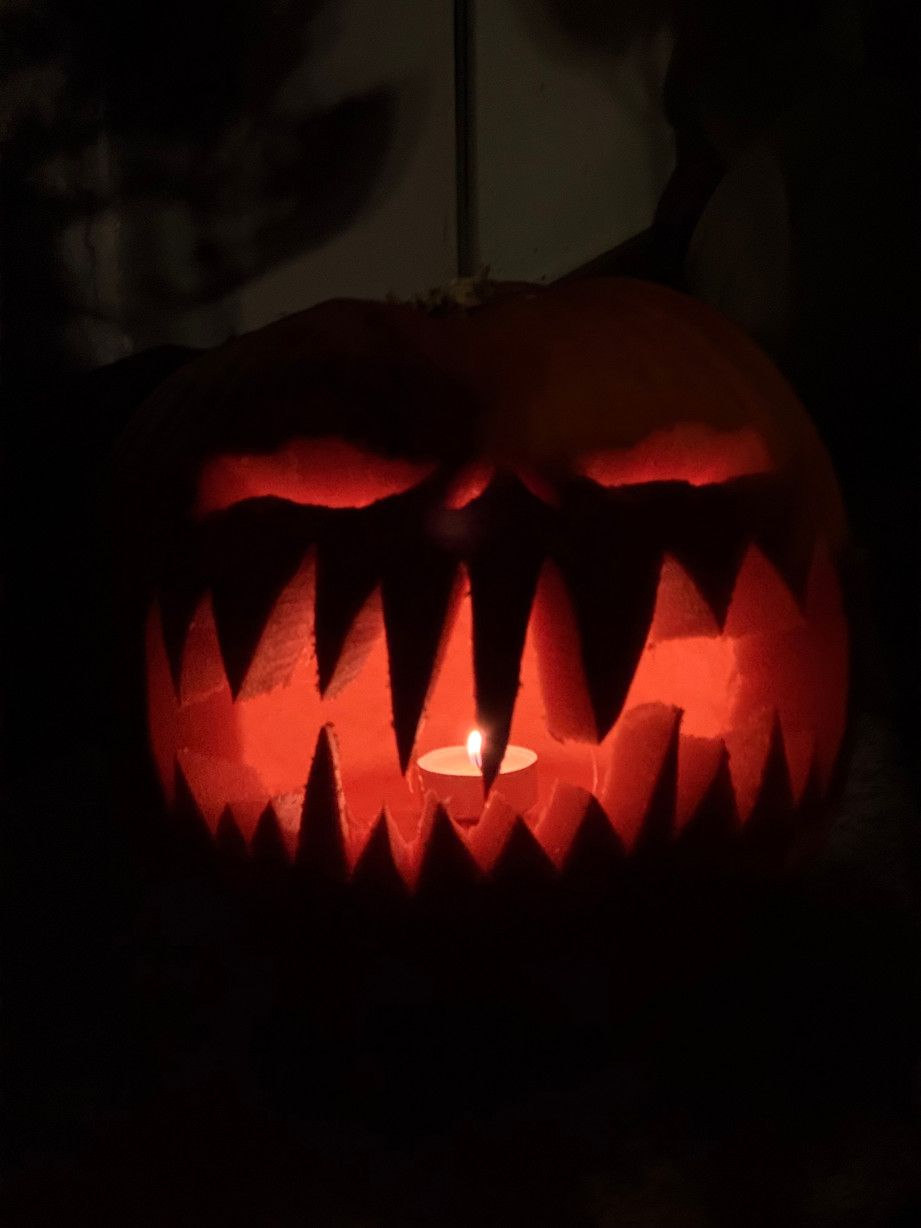 A carved pumpkin with a menacing face is illuminated from within by a candle, casting an eerie glow.