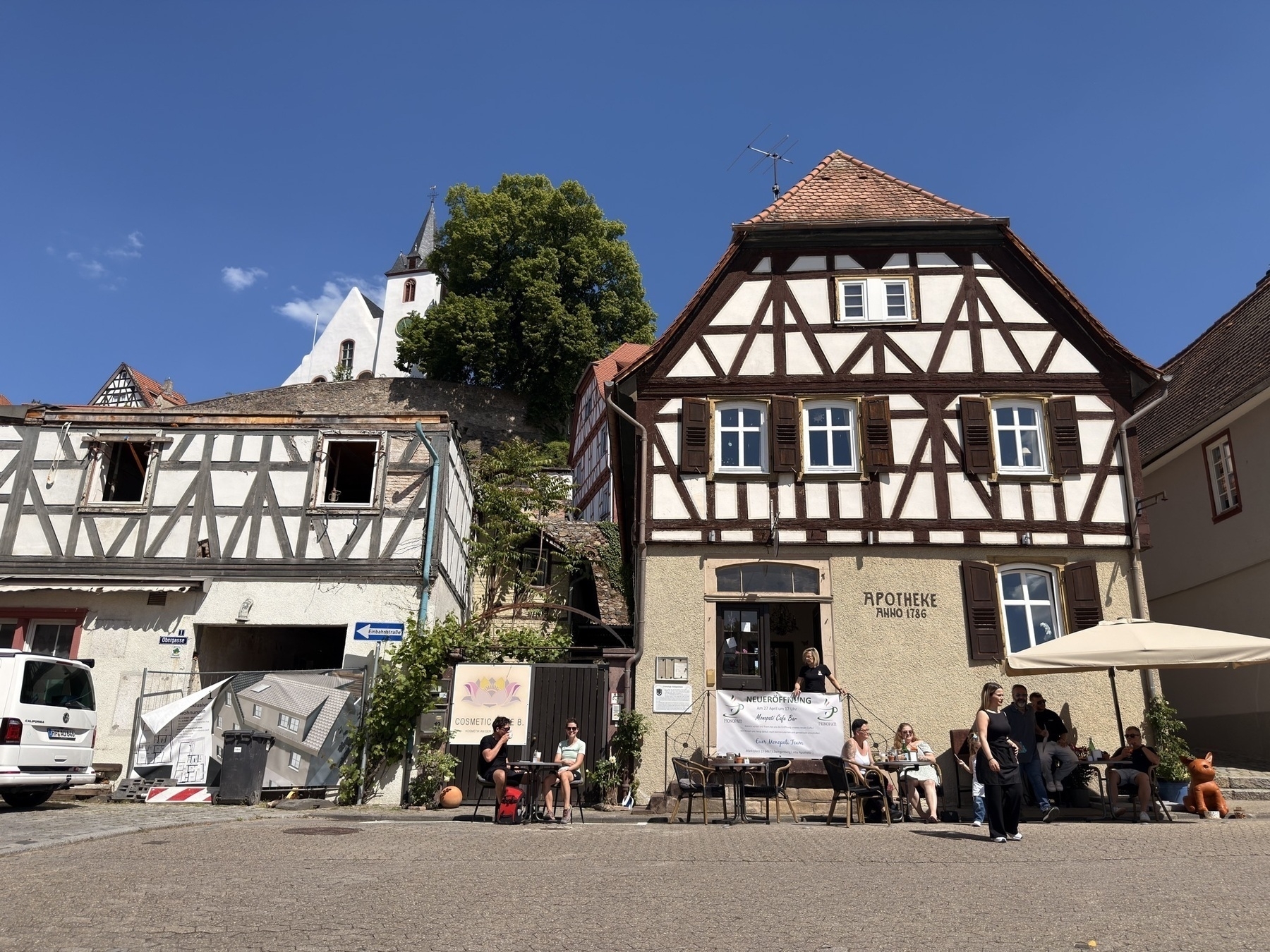 Historic buildings - one a cafe with people sitting outside - on the market square, framed by a clear blue sky. 