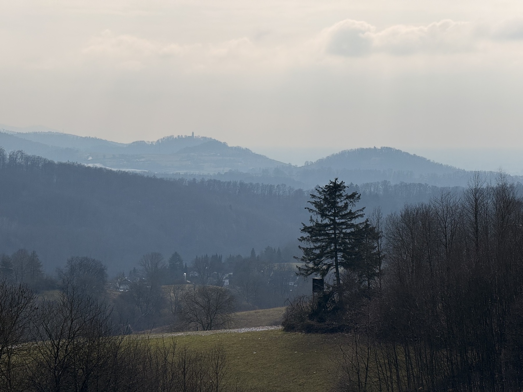 A tranquil landscape features rolling hills, scattered trees, and a cloudy sky.