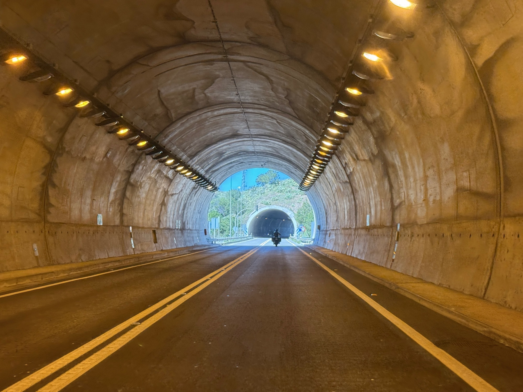 A motorcycle travels through a well-lit tunnel with another tunnel visible in the background.
