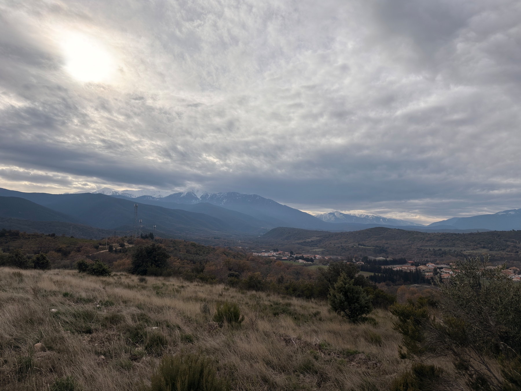 A grassy landscape stretches towards distant mountains under a cloudy sky with patches of sunlight.
