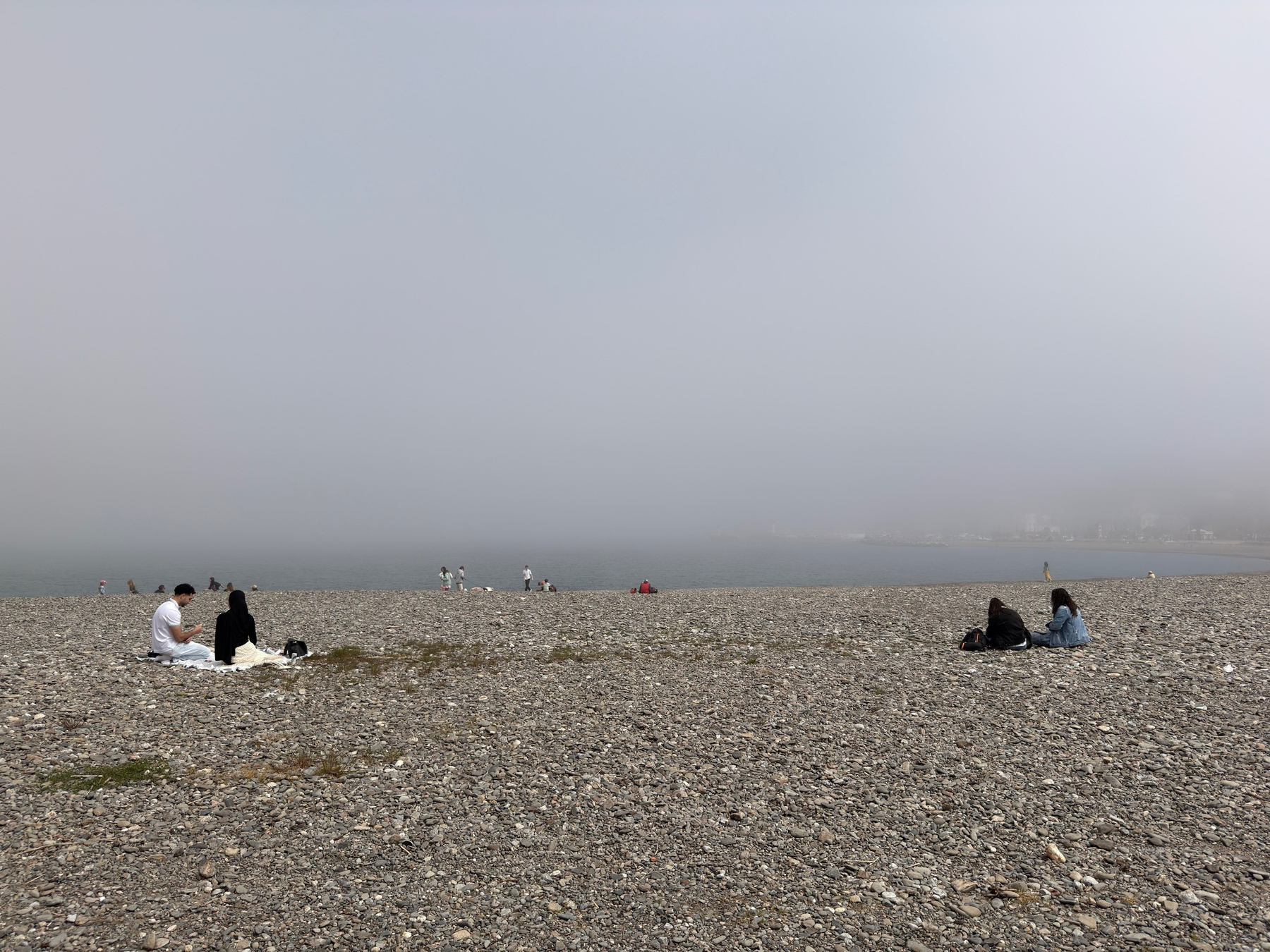 People are sitting on a rocky beach under a foggy sky.