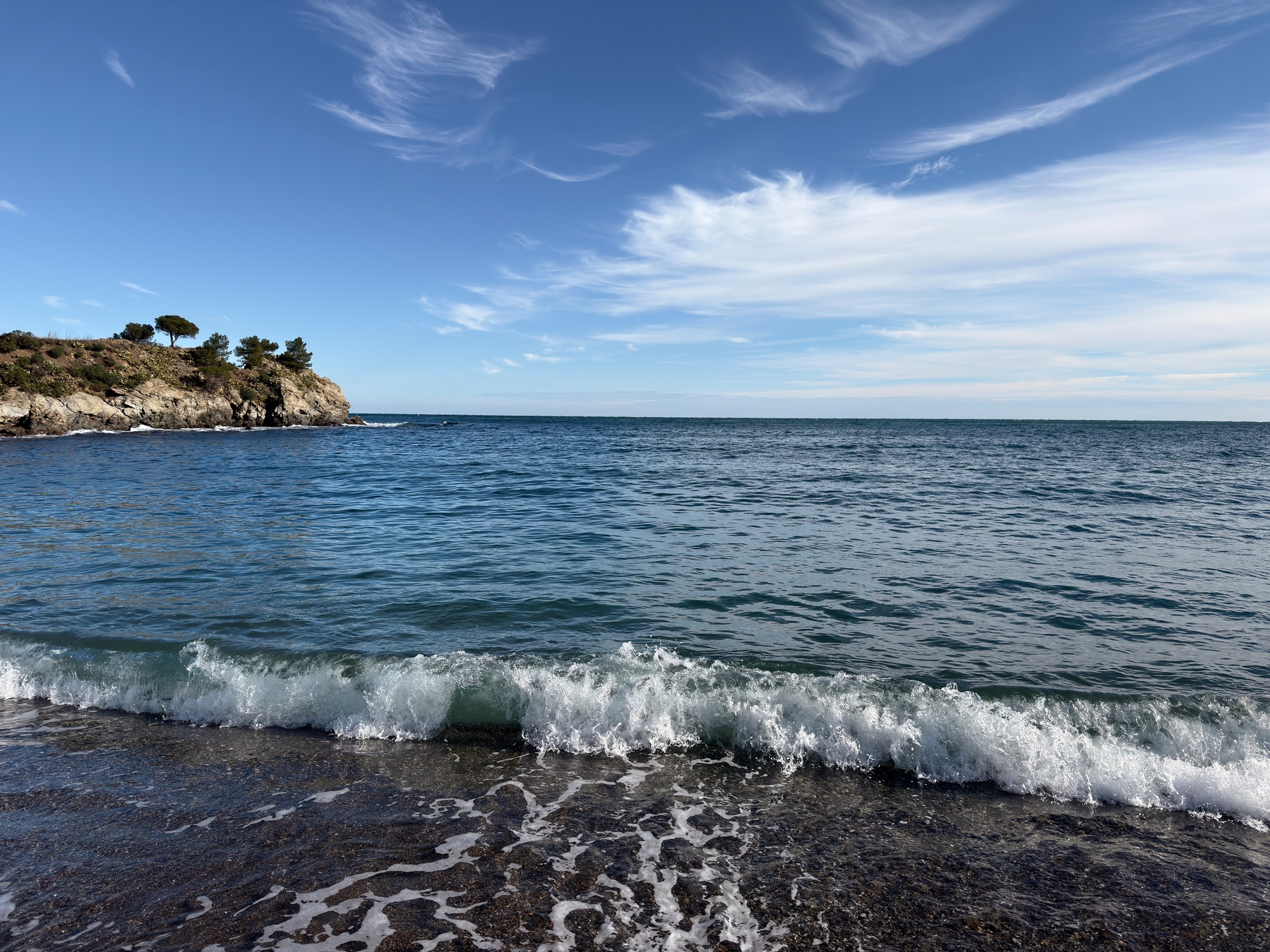 A scenic view of the ocean with gentle waves lapping against the shore under a clear blue sky.