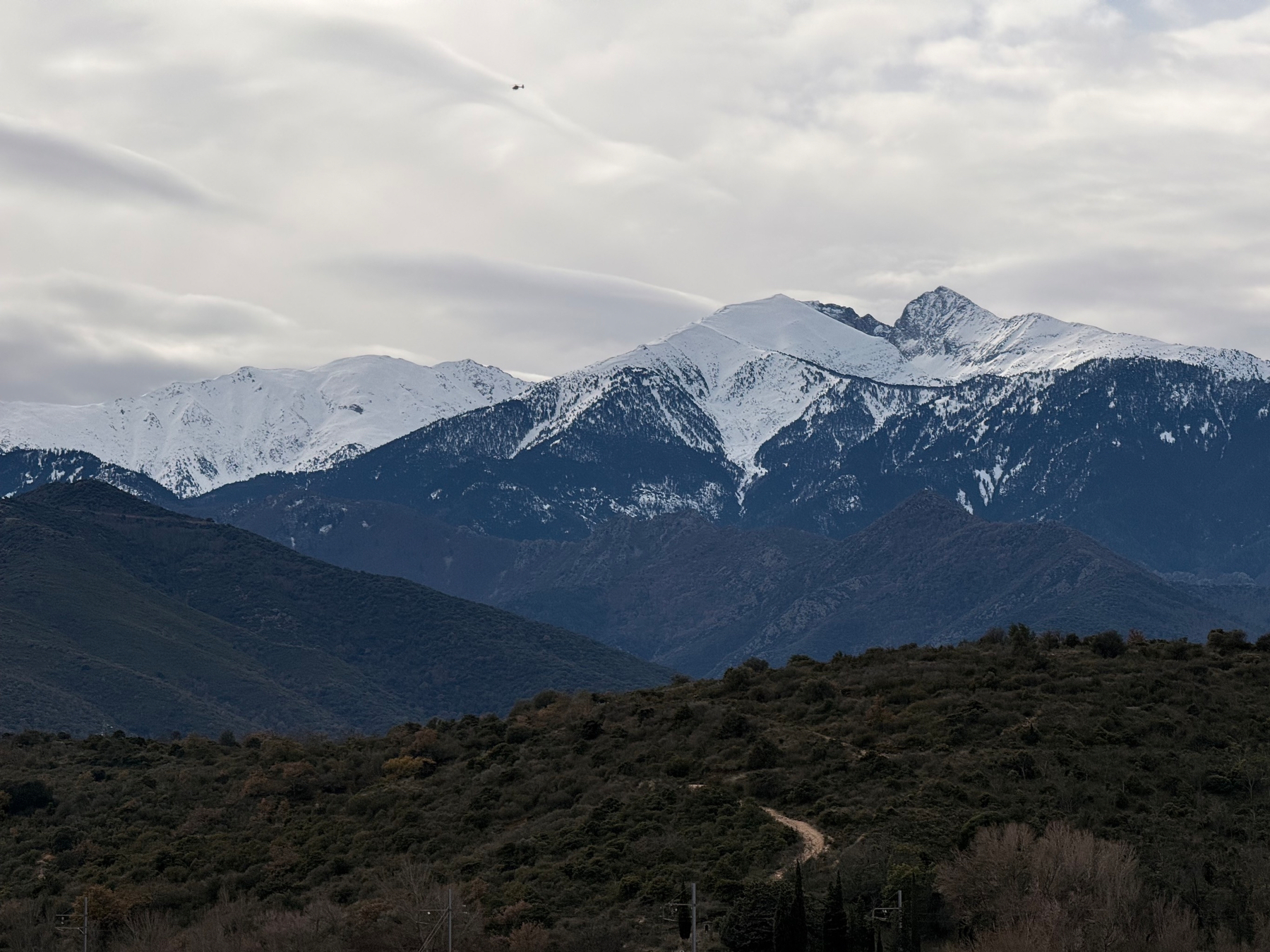 Snow-capped mountains tower over rolling hills under a cloudy sky.