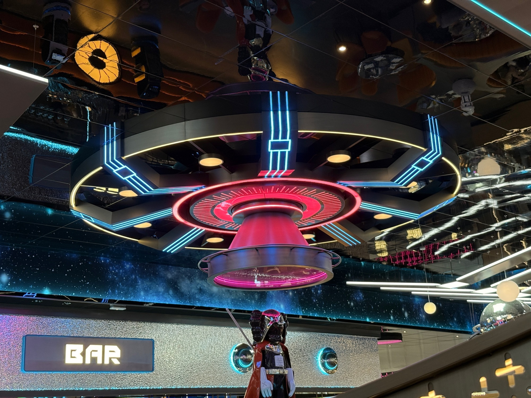 A futuristic, illuminated UFO-themed ceiling decoration is seen above a bar area.